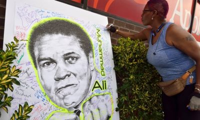 Seorang wanita membubuhkan tanda tangan pada gambar Muhammad Ali di salah satu kota Brooklyn, New York, Amerika. (theguardian.com)