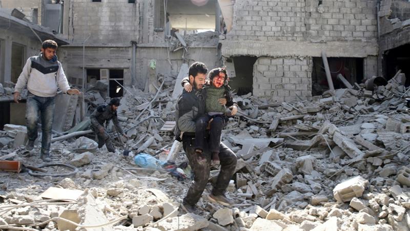 Seorang pria membawa anak laki-laki yang terluka saat ia melewati bangunan-bangunan yang hancur akibat pengeboman di Ghouta Timur, Suriah, Rabu (21/2). (Foto: Reuters/Al Jazeera)