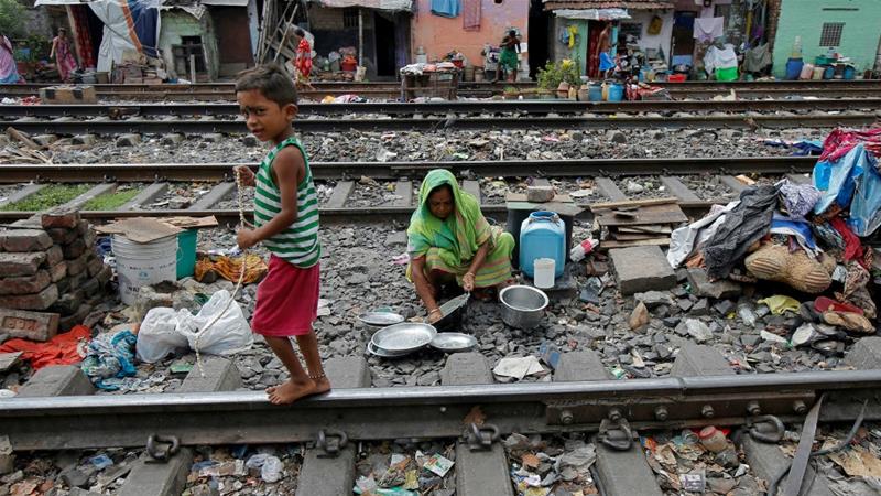 Seorang anak laki-laki meeniti rel melewati seorang wanita yang membersihkan peralatan dapurnya di antara rel kereta api di daerah kumuh Kalkuta, India. (Foto:Reuters/Al Jazeera)