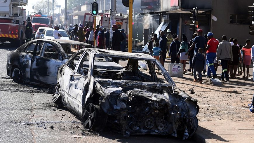 Pejalan kaki melewati mobil-mobil yang terbakar di sisi jalan di pinggiran Johannesburg pada hari Senin (2/9). (Foto: AP/Al Jazeera)