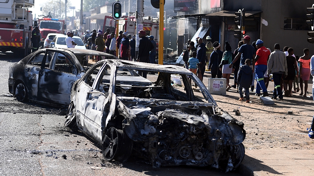Pejalan kaki melewati mobil-mobil yang terbakar di sisi jalan di pinggiran Johannesburg pada hari Senin (2/9). (Foto: AP/Al Jazeera)