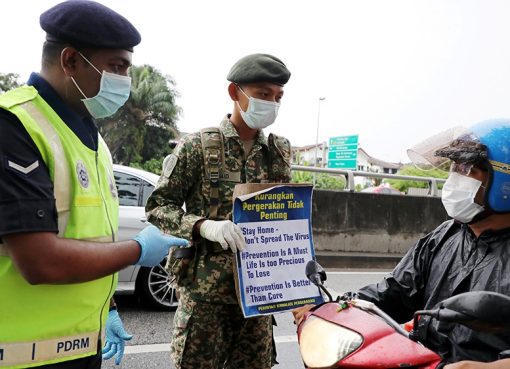 Seorang tentara dan seorang polisi menunjukkan plakat pembertahuan kepada pengendara sepeda motor di sebuah pos yang didirikan untuk menegakkan perintah gerakan kontrol di Kuala Lumpur, Malaysia. (Foto: Reuters/Al Jazeera)