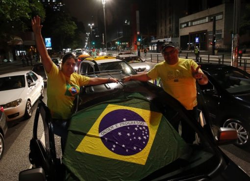 Pendukung Presiden Jair Bolsonaro mengibarkan bendera Brasil ketika mereka mengambil bagian dalam iring-iringan mobil untuk memprotes tindakan karantina dan jarak sosial untuk memerangi wabah virus corona baru pada 18 April 2020, di Sao Paulo. (Foot: Getty Images/Al Jazeera)