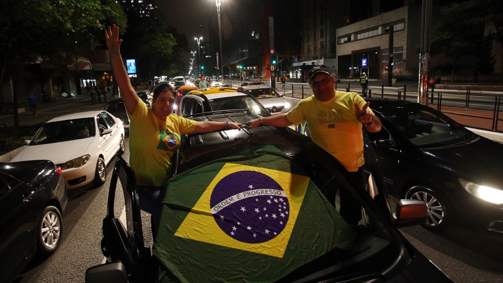 Pendukung Presiden Jair Bolsonaro mengibarkan bendera Brasil ketika mereka mengambil bagian dalam iring-iringan mobil untuk memprotes tindakan karantina dan jarak sosial untuk memerangi wabah virus corona baru pada 18 April 2020, di Sao Paulo. (Foot: Getty Images/Al Jazeera)