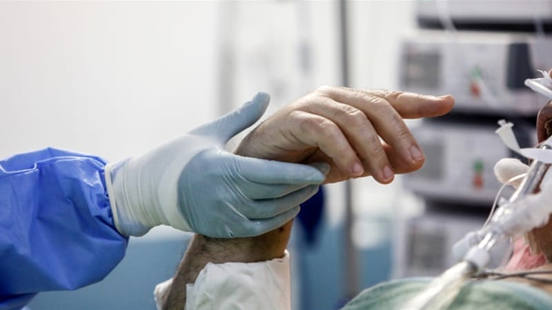 Seorang pasien yang diintubasi berusaha memberi isyarat pada seorang pekerja medis yang memegang tangannya di unit perawatan intensif (ICU) rumah sakit Sotiria di Athena, Yunani.(Foto: Reuters/Al Jazeera)