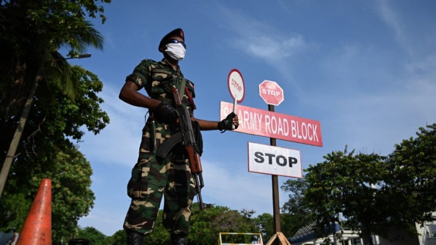Seorang personil militer Sri Lanka yang mengenakan masker wajah memegang tanda berhenti di sebuah pos pemeriksaan selama penguncian nasional yang diberlakukan pemerintah, sebagai langkah pencegahan terhadap wabah COVID-19 di Kolombo pada 29 April 2020. (Fot: AFP/Al Jazeera)