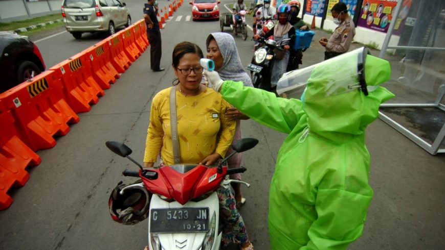 Seorang petugas medis yang mengenakan pakaian pelindung, memeriksa seorang wanita dengan pemindai termal di tengah wabah penyakit corona (COVID-19), di Tegal, Jawa Tengah.(Foto: Reuters/Al Jazeera)