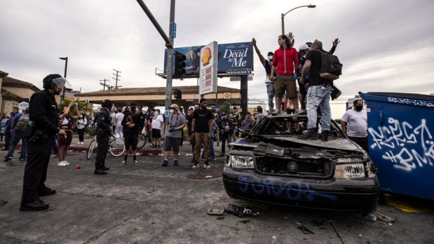 Para pengunjuk rasa berdiri di atas sebuah mobil polisi yang telah terbakar di Los Angeles, California.(Foto: EPA/BBC News)