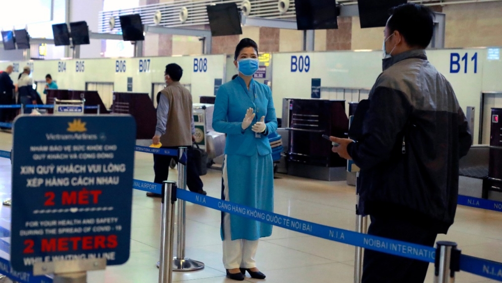 Seorang staf maskapai penerbangan menginstruksikan kepada penumpang bagaimana cara check in di bandara Hanoi, Vietnam, sambil menjaga jarak sosial. (Fot: AP/Al Jazeera)
