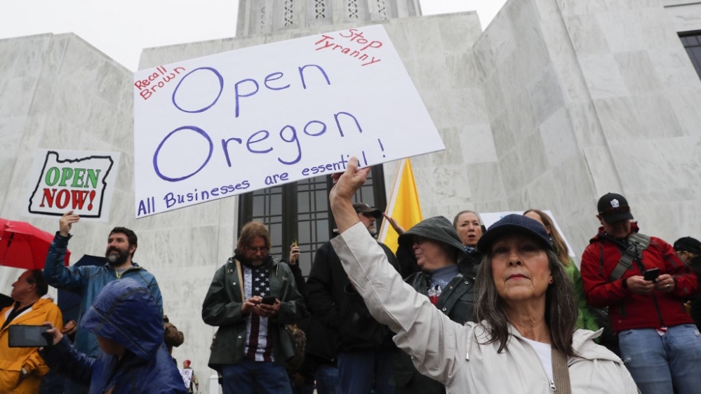 Seorang wanita memegang pamflet bertuliskan Open Oregon di tangga ibukota negara bagian di kota Salem Oregon, pada 2 Mei 2020.( Foto: Getty Images/AFP/Al Jazeera)