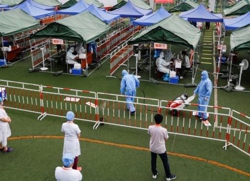 Seorang pekerja dalam pakaian pelindung menyemprotkan desinfektan ketika pekerja medis melakukan tes asam nukleat di sebuah lokasi pengujian di Beijing. (Foto Reuters/Al Jazeera)