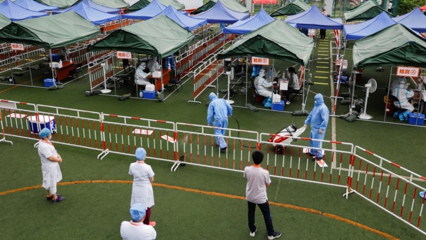 Seorang pekerja dalam pakaian pelindung menyemprotkan desinfektan ketika pekerja medis melakukan tes asam nukleat di sebuah lokasi pengujian di Beijing. (Foto Reuters/Al Jazeera)